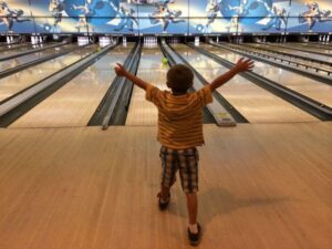 Child with hands in air after releasing their bowling ball down an alley at Rab’s Country Lanes