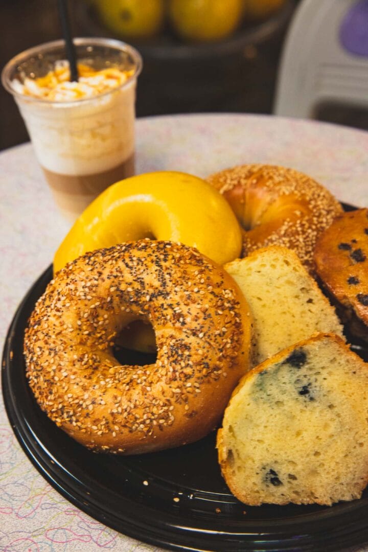 A plate with assorted bagels, including everything and blueberry, sits next to an iced coffee topped with whipped cream and caramel drizzle.