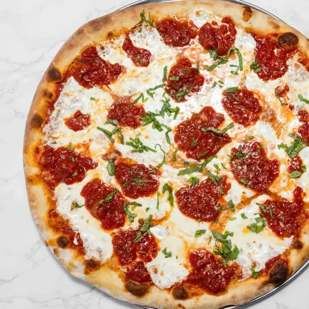 A round pizza topped with melted mozzarella cheese, tomato sauce, and sliced fresh basil on a thin, lightly browned crust.
