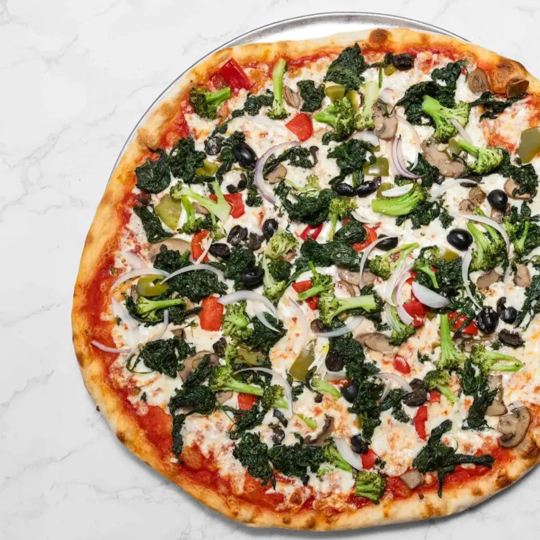 Large pizza topped with spinach, broccoli, black olives, onions, mushrooms, bell peppers, and melted cheese on a marble surface.