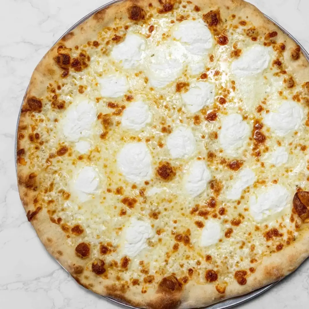 A cheese pizza with a golden crust, topped with melted mozzarella and dollops of ricotta cheese, on a round metal tray.